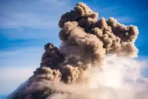 Hiker on volcanic mountain ridge during storm with ash clouds