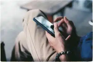 Hands holding a smartphone with social media feed scrolling on screen in dim lighting