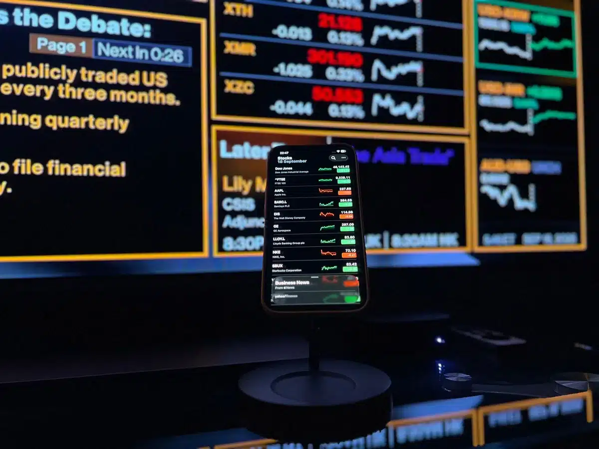 A child's hand interacting with a digital investment interface showing stock charts and savings growth on a screen