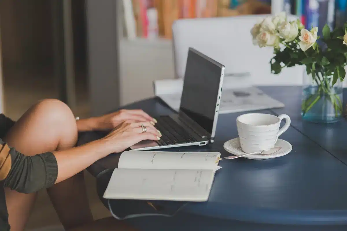 Mug of coffee beside an open laptop and phone on a kitchen table, morning light