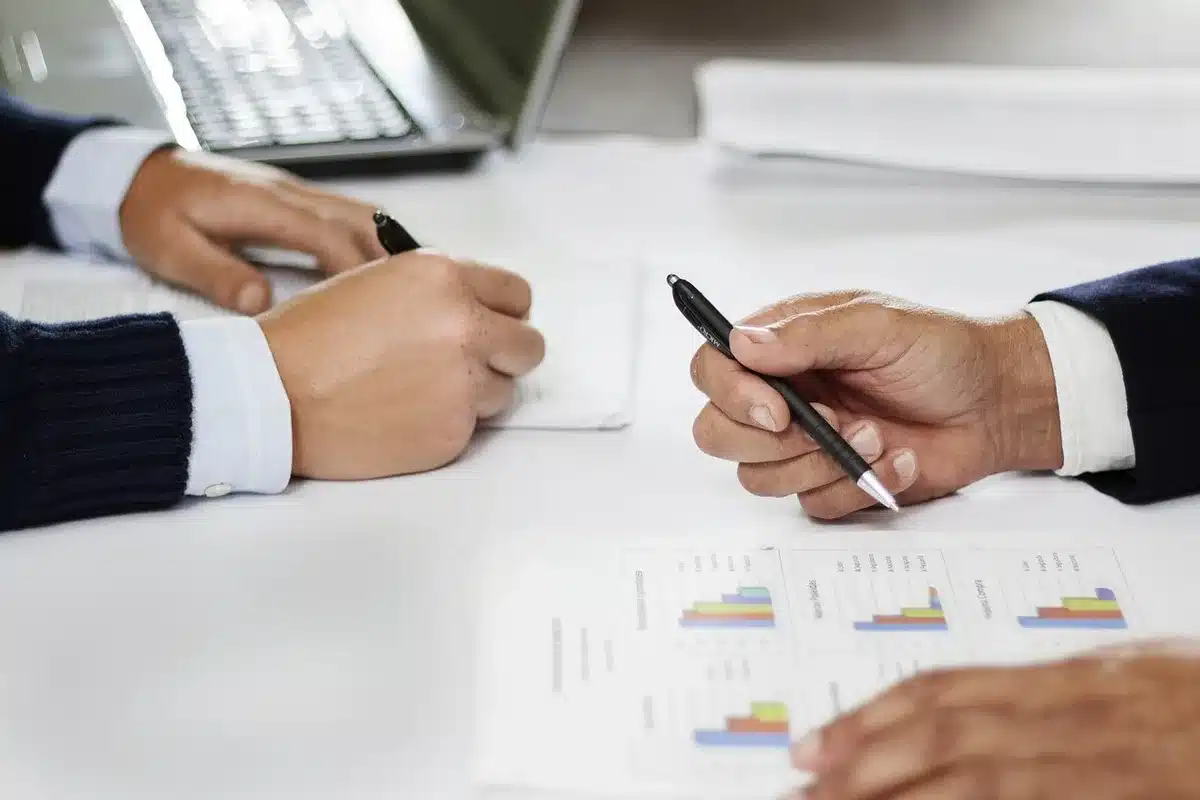 Hands holding health plan documents and a binder on a conference table with blurred silhouettes