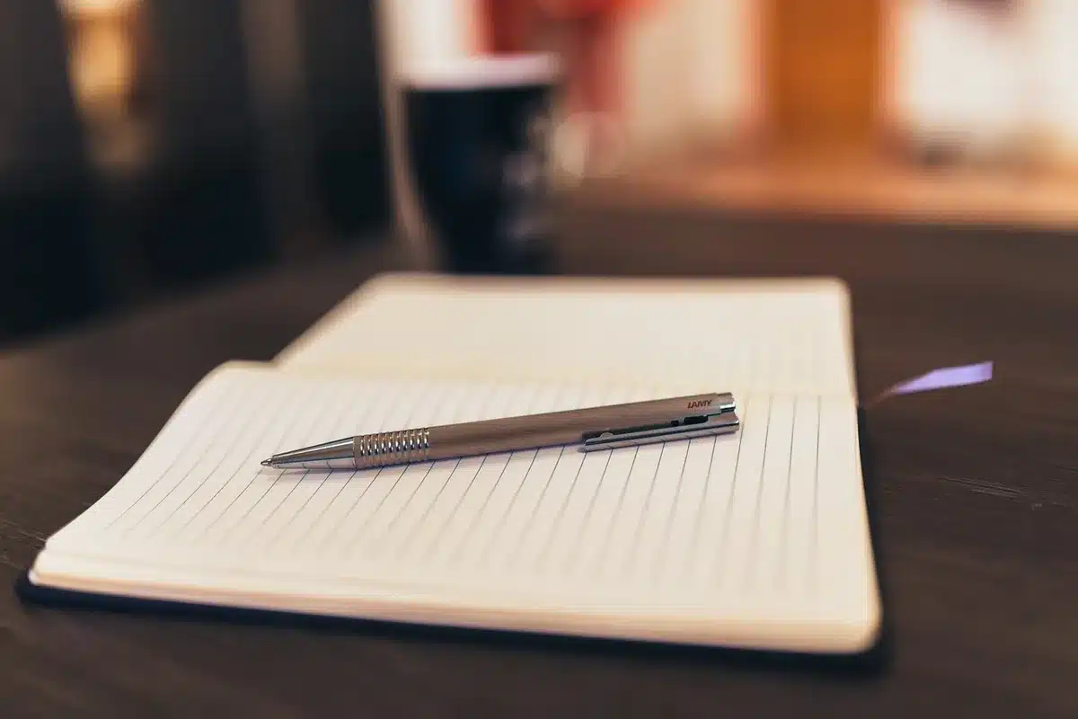 Hand writing in a notebook with pen on a clear desk, morning light
