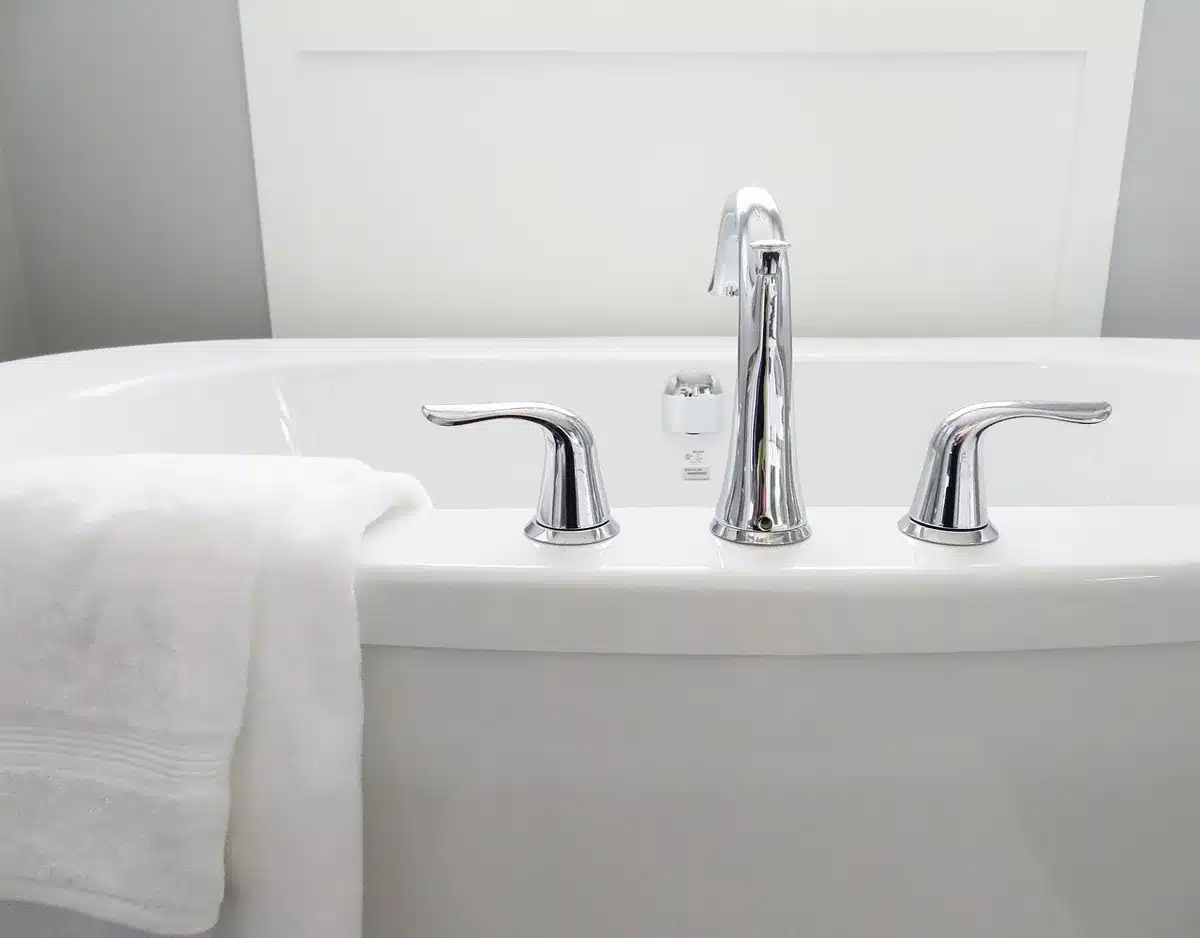Steaming bathtub with towel and thermometer on a shelf in a bright bathroom