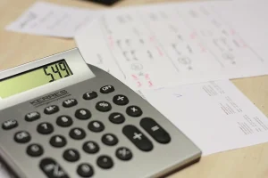 Hands with bills, calculator, car key and house key on a kitchen table