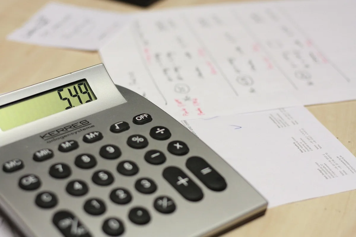 Hands with bills, calculator, car key and house key on a kitchen table